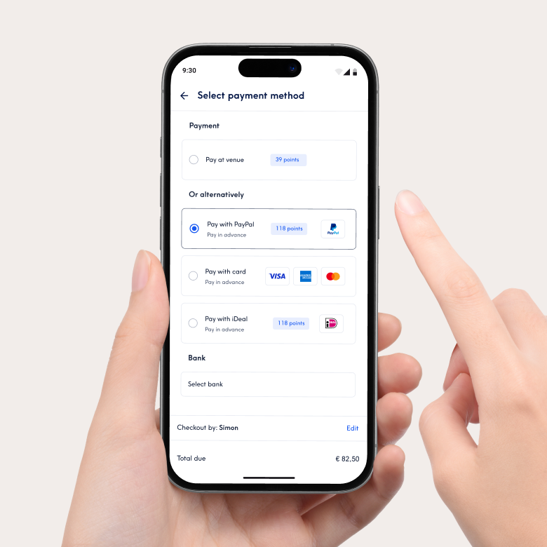 Κοντινό πλάνο ενός smartphone που δείχνει τη διεπαφή πληρωμής της εφαρμογής Treatwell για την επιλογή μεθόδου πληρωμής. Οι επιλογές περιλαμβάνουν πληρωμή στον χώρο ή προπληρωμή με PayPal, κάρτα ή iDeal. Ένα χέρι κρατά το τηλέφωνο και ένα δάχτυλο δείχνει την οθόνη.