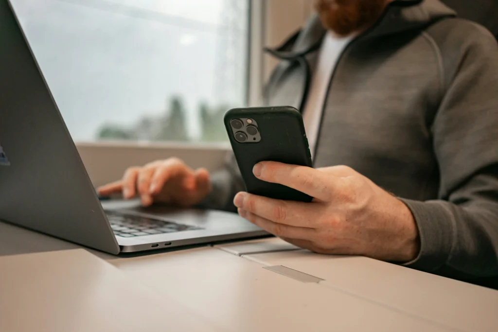 Ένας ιδιοκτήτης σαλονιού διαχειρίζεται online ραντεβού στο κινητό ενώ χρησιμοποιεί laptop