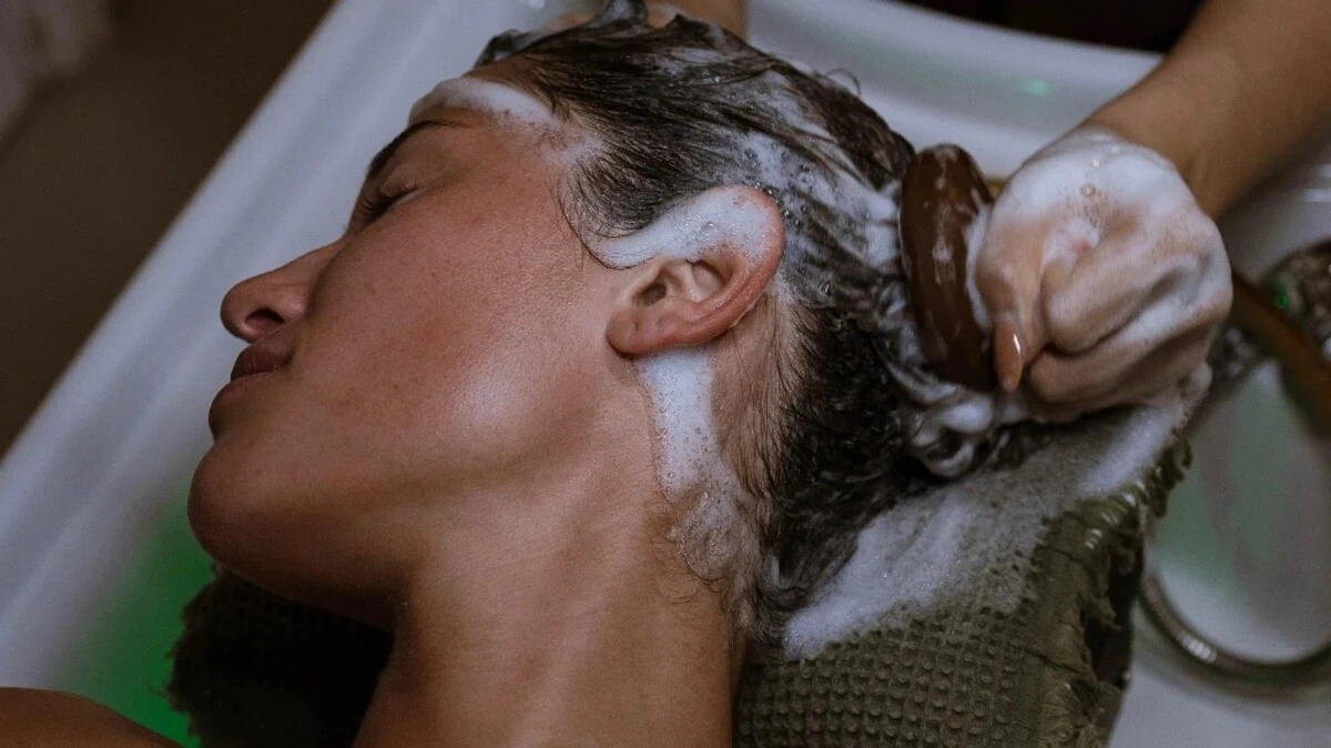 Κοντινό πλάνο ειδικού που εκτελεί ένα Japanese Head Spa με βούρτσα τριχωτού σε μια πελάτισσα