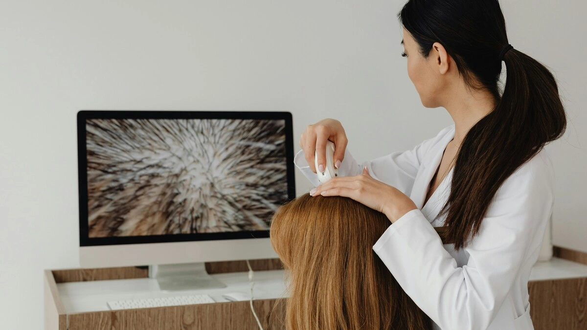 Ένας ειδικός εξετάζει το τριχωτό μιας πελάτισσας με κάμερα υψηλής ανάλυσης και δείχνει την εικόνα σε μια μεγάλη οθόνη