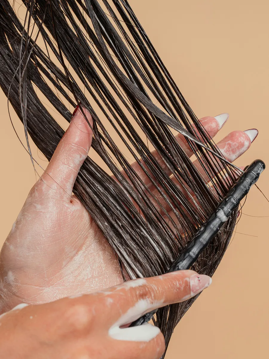 Κοντινή λήψη γυναίκας που απλώνει conditioner στα μακριά μαλλιά της με χτένα με αραιά δόντια