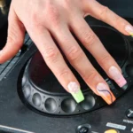 Ένα χέρι με το electric mani ακουμπισμένο στο jog wheel ενός DJ player Pioneer, με neon french tips σε animal print και σπιράλ