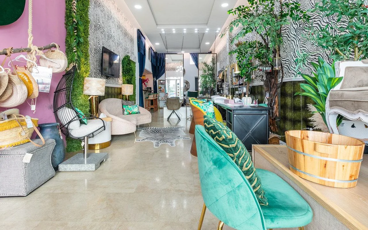 Το εσωτερικό της Brazilian Beauty Marbella, ένα φωτεινό σαλόνι με τοίχους σε μοτίβο ζέβρας, έναν τοίχο με φυτά, τιρκουάζ βελούδινες καρέκλες και μια ξύλινη λεκάνη πεντικιούρ.