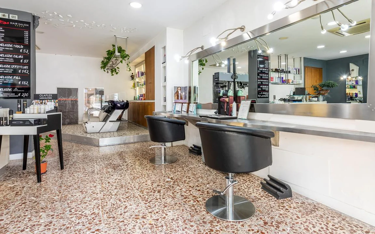 Το εσωτερικό του Hair Salon Luigi Zito, με δάπεδο terrazzo, δύο μαύρες καρέκλες χτενίσματος μπροστά από έναν μακρύ καθρέφτη, πίνακες τιμών από κιμωλία στον τοίχο, μια προθήκη προϊόντων και έναν νιπτήρα κεφαλής στο βάθος.