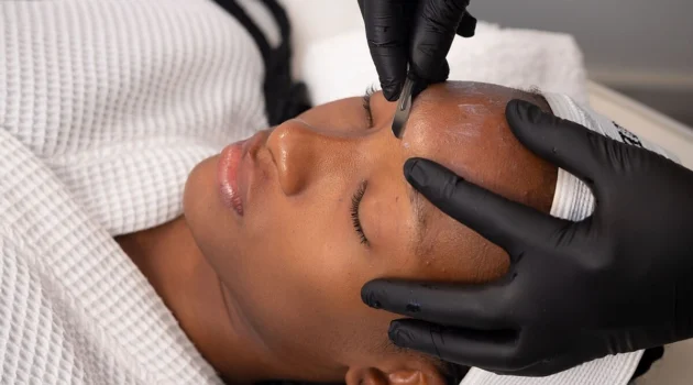 Κοντινό πλάνο μιας αισθητικού που κάνει dermaplaning σε μια πελάτισσα σε κέντρο αισθητικής