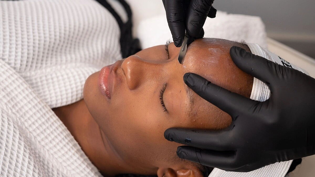 Κοντινό πλάνο μιας αισθητικού που κάνει dermaplaning σε μια πελάτισσα σε κέντρο αισθητικής